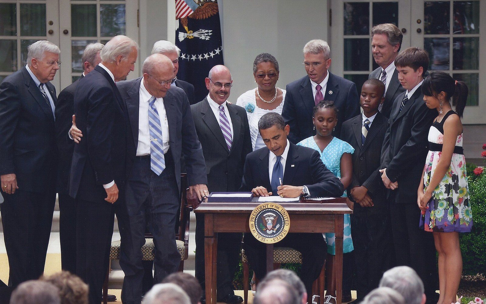 President signs legislation at an outdoor desk surrounded by officials and onlookers