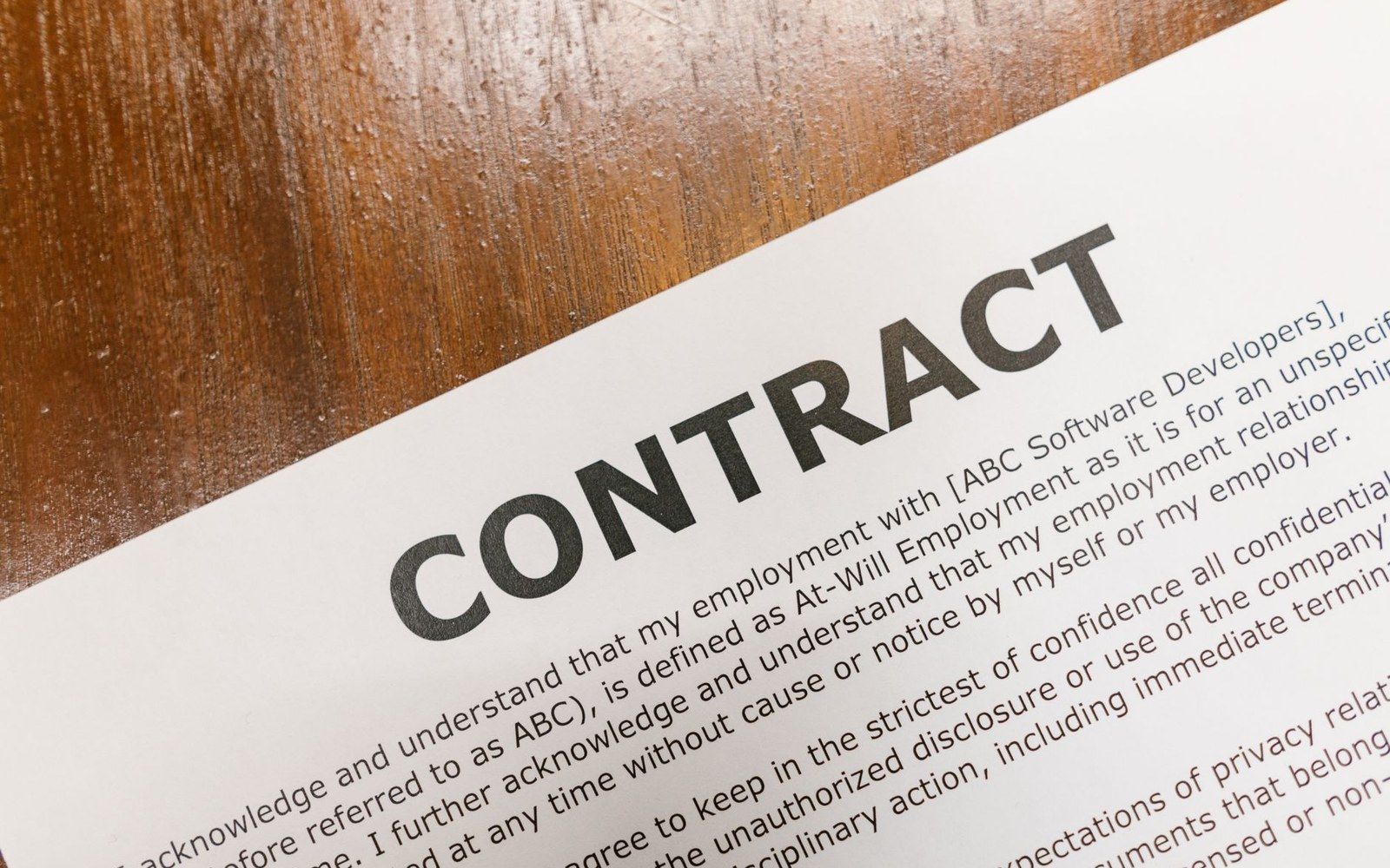 A printed employment contract document lying on a wooden table surface