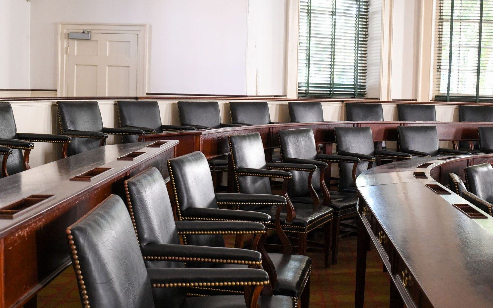 Empty leather chairs arranged in curved rows around wooden tables in a hearing room