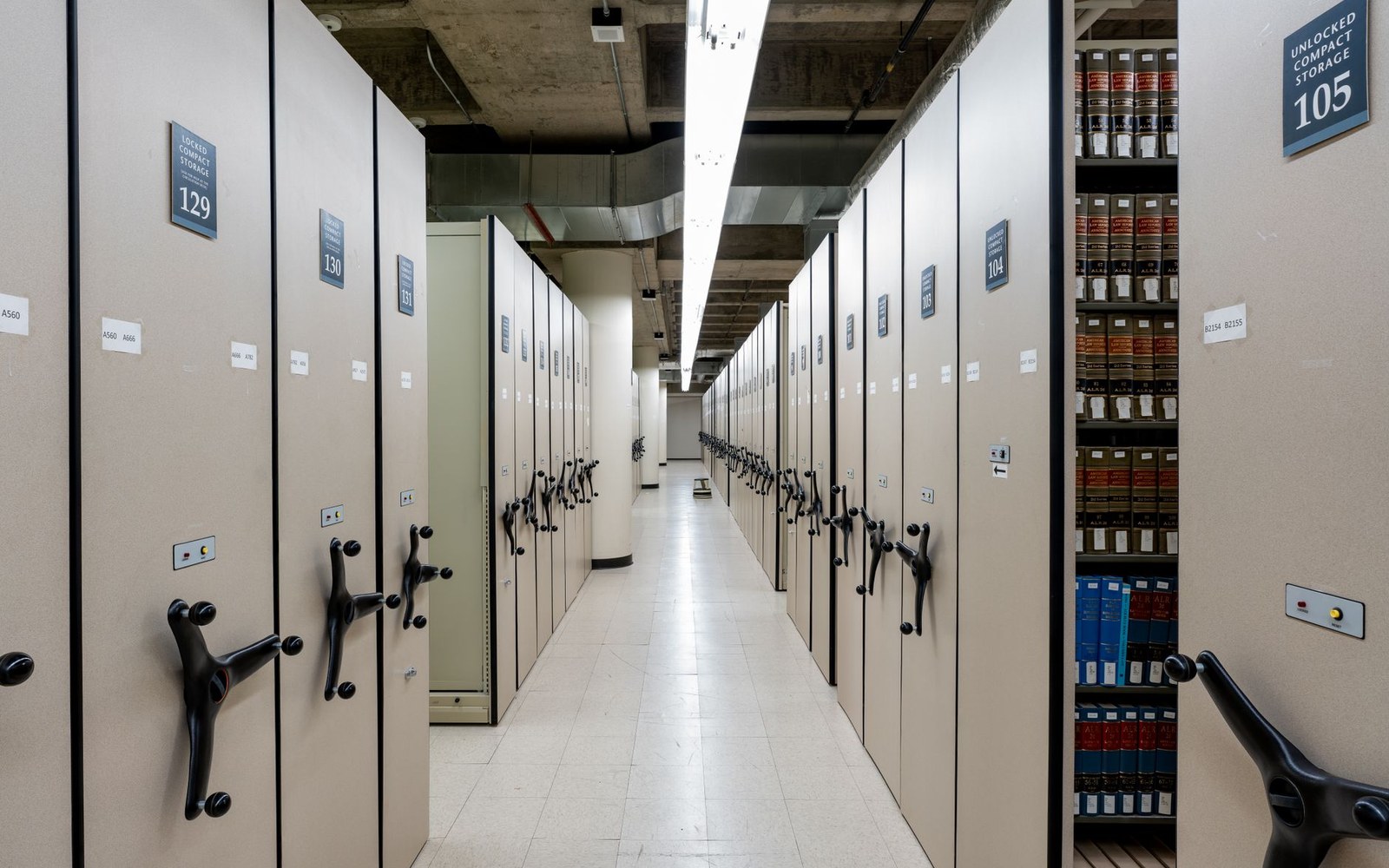 Rows of numbered compact mobile shelving units with crank handles in an archive storage room
